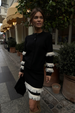 model is wearing a black cardigan and skirt with cream fringe detailing on the sleeves and skirt hem